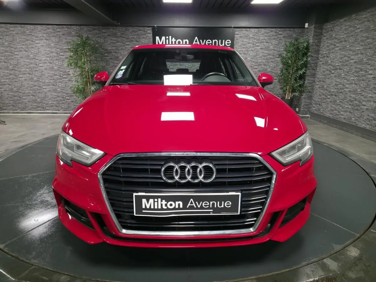Vue avant d'une Audi A3 Sportback rouge avec calandre noire et logo Audi, en intérieur showroom.