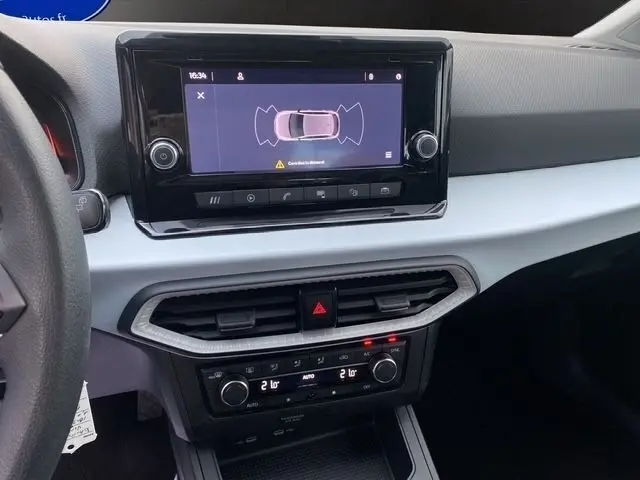 Vue intérieure du tableau de bord blanc de la SEAT Ibiza 2023, avec écran tactile central affichant l'aide au stationnement.