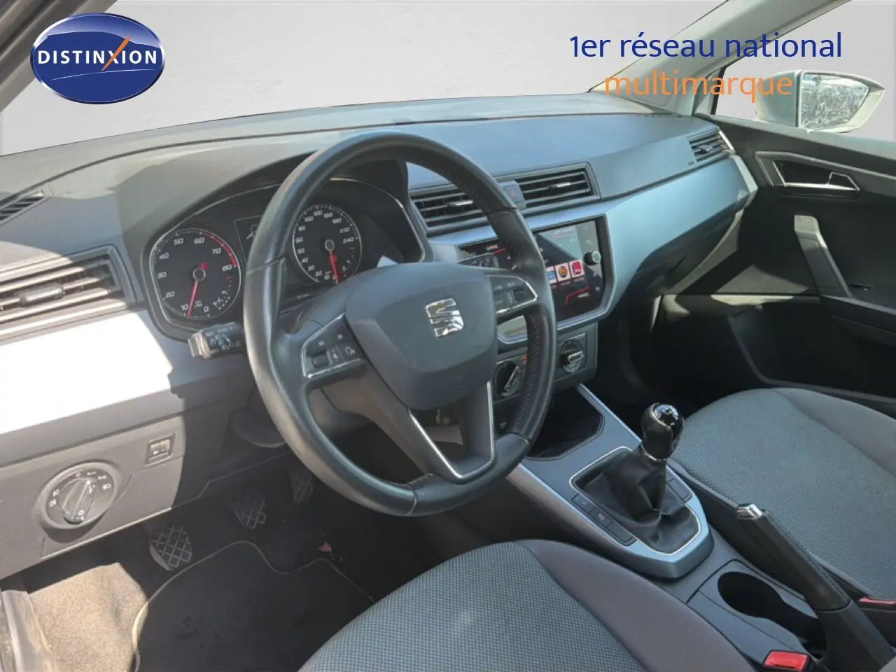 Vue intérieure côté conducteur du tableau de bord et levier de vitesses manuel d'une SEAT Arona 2018 avec sellerie tissu grise.