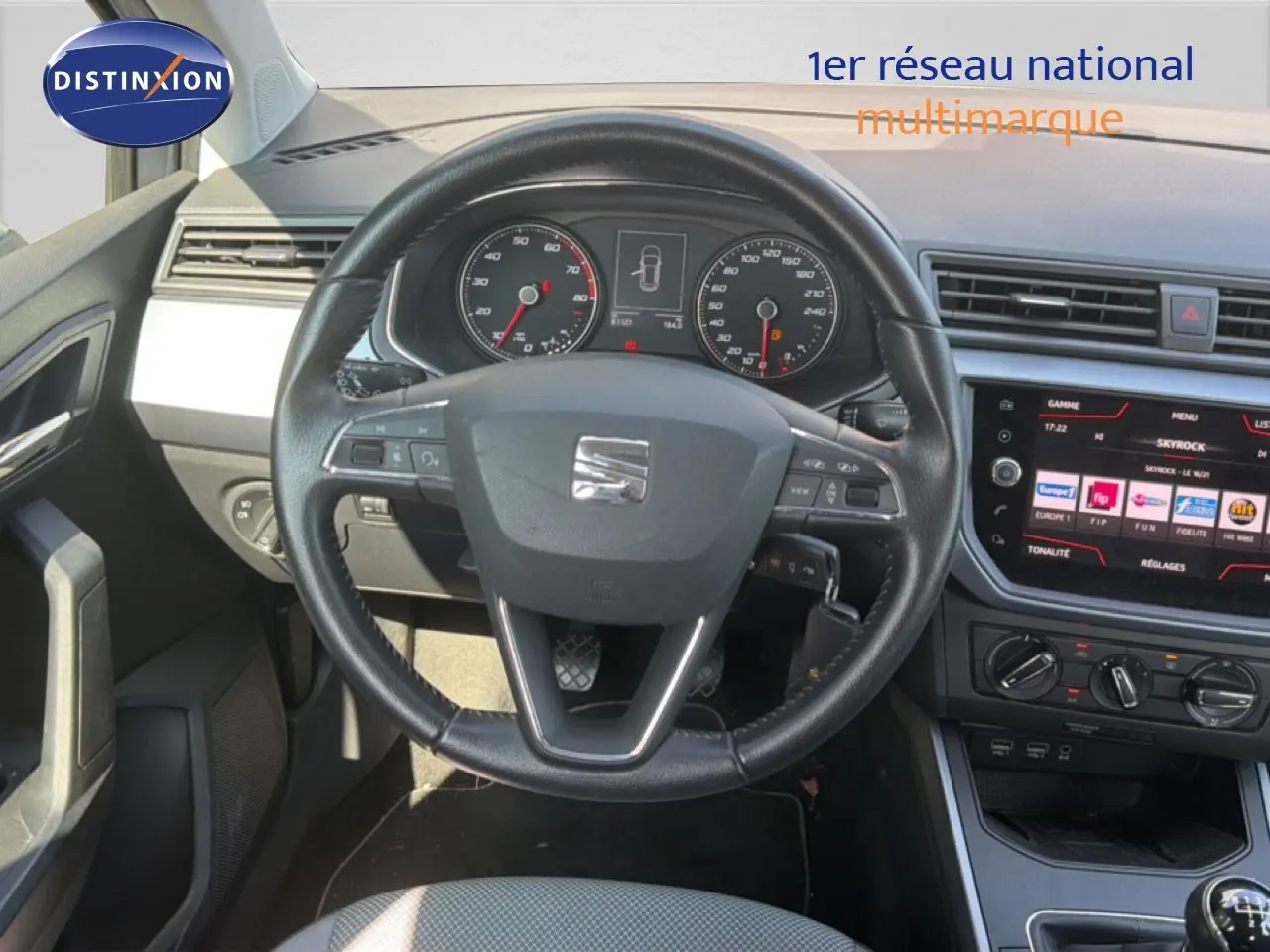 Vue intérieure centrée sur le volant et le tableau de bord d'une SEAT Arona gris urbain avec écran tactile et commandes au volant.