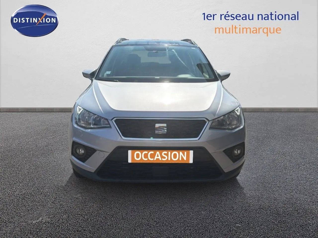 Vue frontale d'une SEAT Arona gris urbain avec calandre noire et plaque "OCCASION" visible sur un sol bitumé.