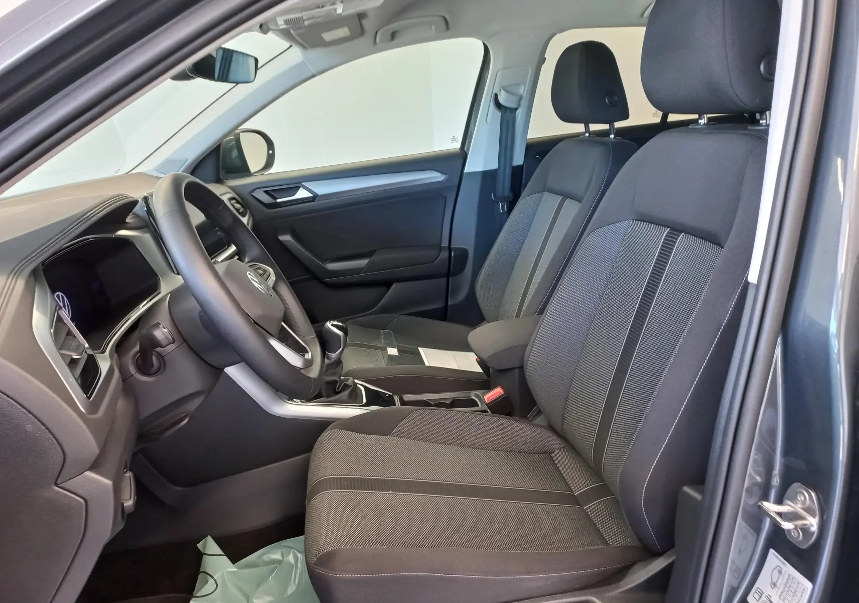 Vue intérieure côté conducteur du Volkswagen T-Roc 2025 gris Indium, montrant les sièges et le volant avec boîte manuelle.