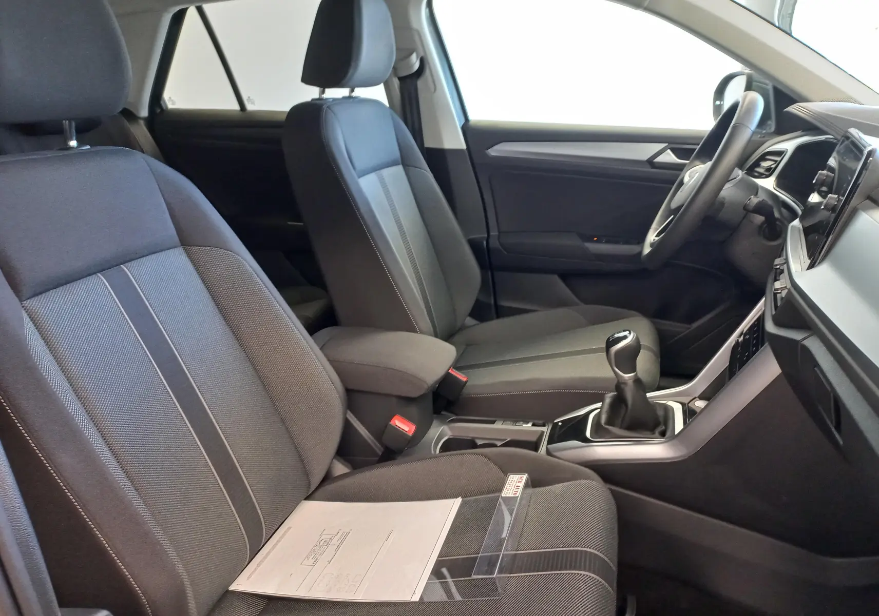 Vue intérieure côté conducteur du Volkswagen T-Roc 2025, sièges gris foncé avec console centrale et levier de vitesses manuel.