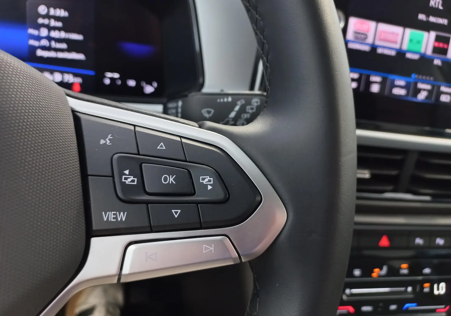 Gros plan sur les commandes au volant côté gauche du Volkswagen T-Roc 2025, avec écran digital en arrière-plan flou.