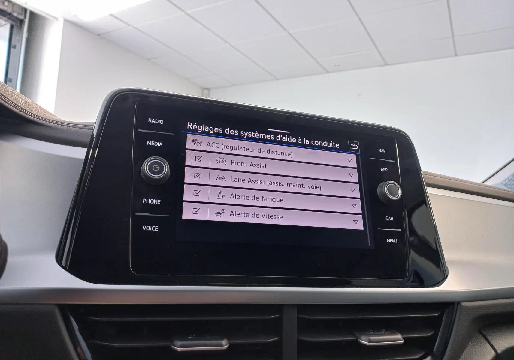 Écran tactile central du Volkswagen T-Roc 2025 affichant les réglages des aides à la conduite dans un intérieur clair.