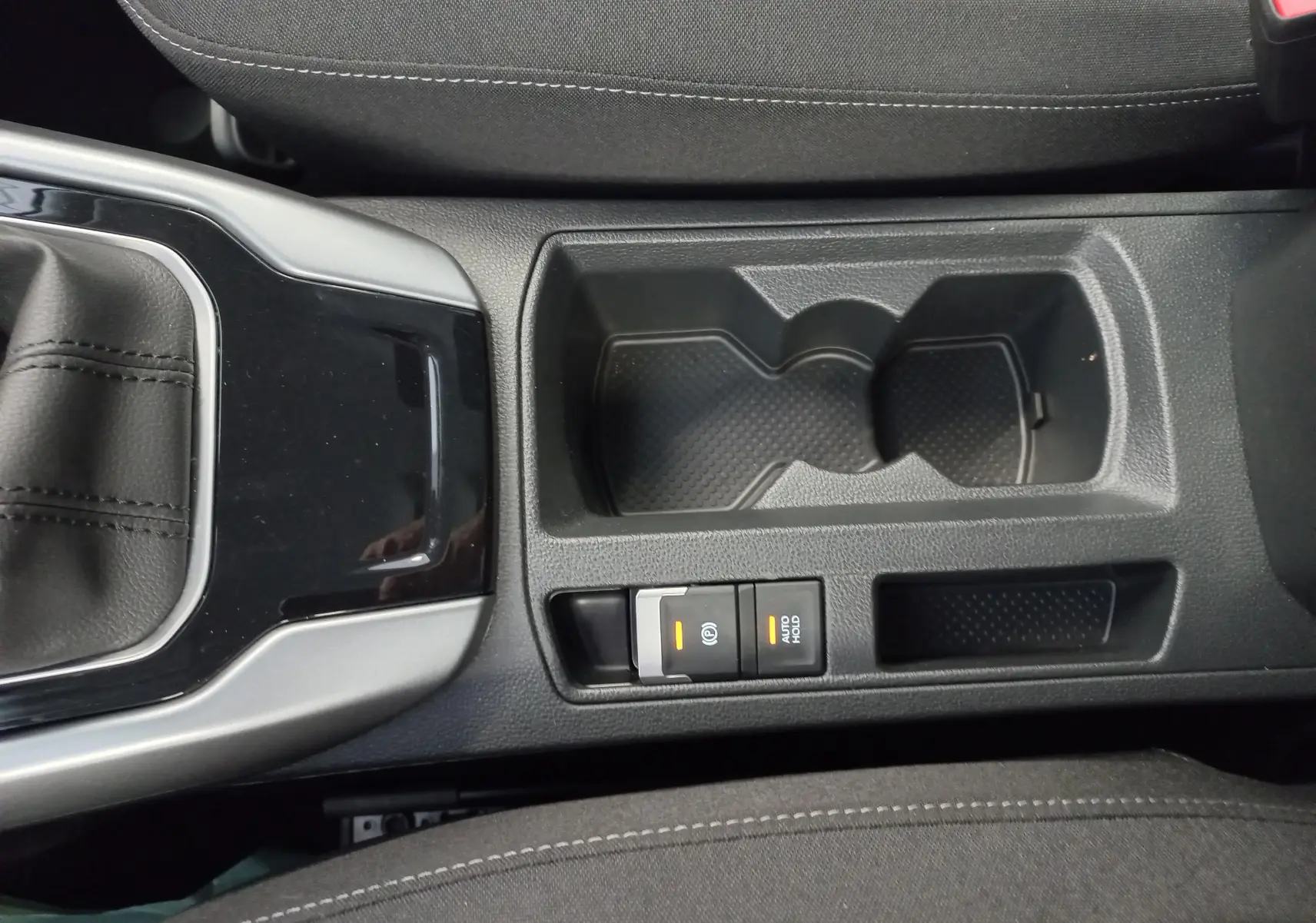 Vue rapprochée de la console centrale du Volkswagen T-Roc 2025, montrant le porte-gobelets et les commandes de frein à main électrique.