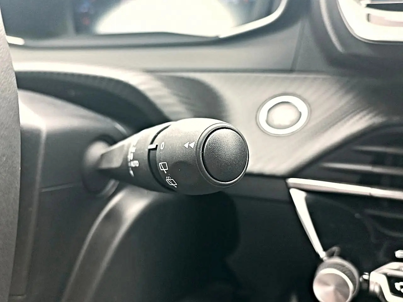 Gros plan sur la commande d’essuie-glace à gauche du volant dans l’habitacle noir du Peugeot 2008 Rouge Elixir.
