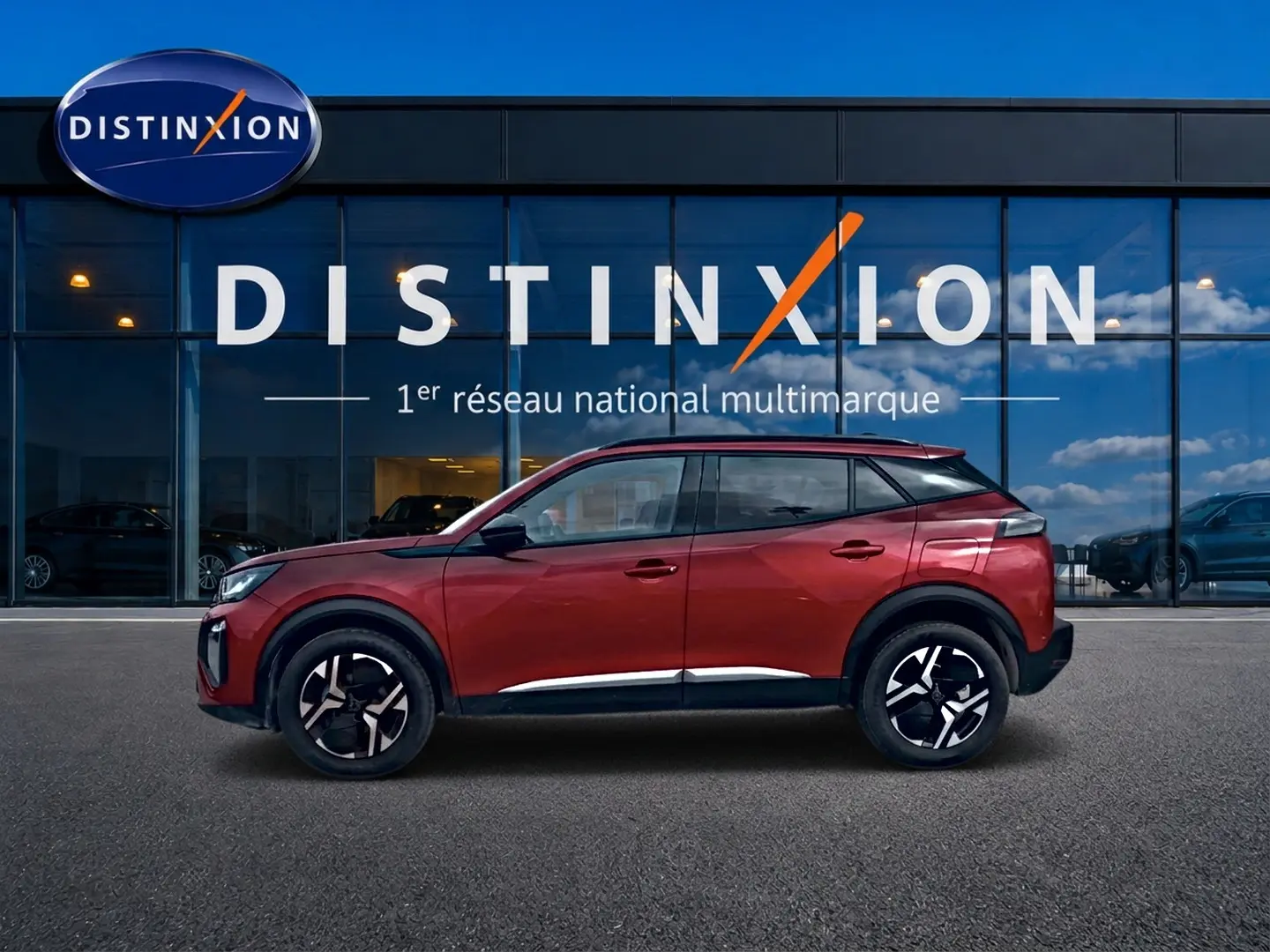 Profil latéral gauche d'un Peugeot 2008 rouge elixir avec jantes alu noires devant une vitrine Distinxion.