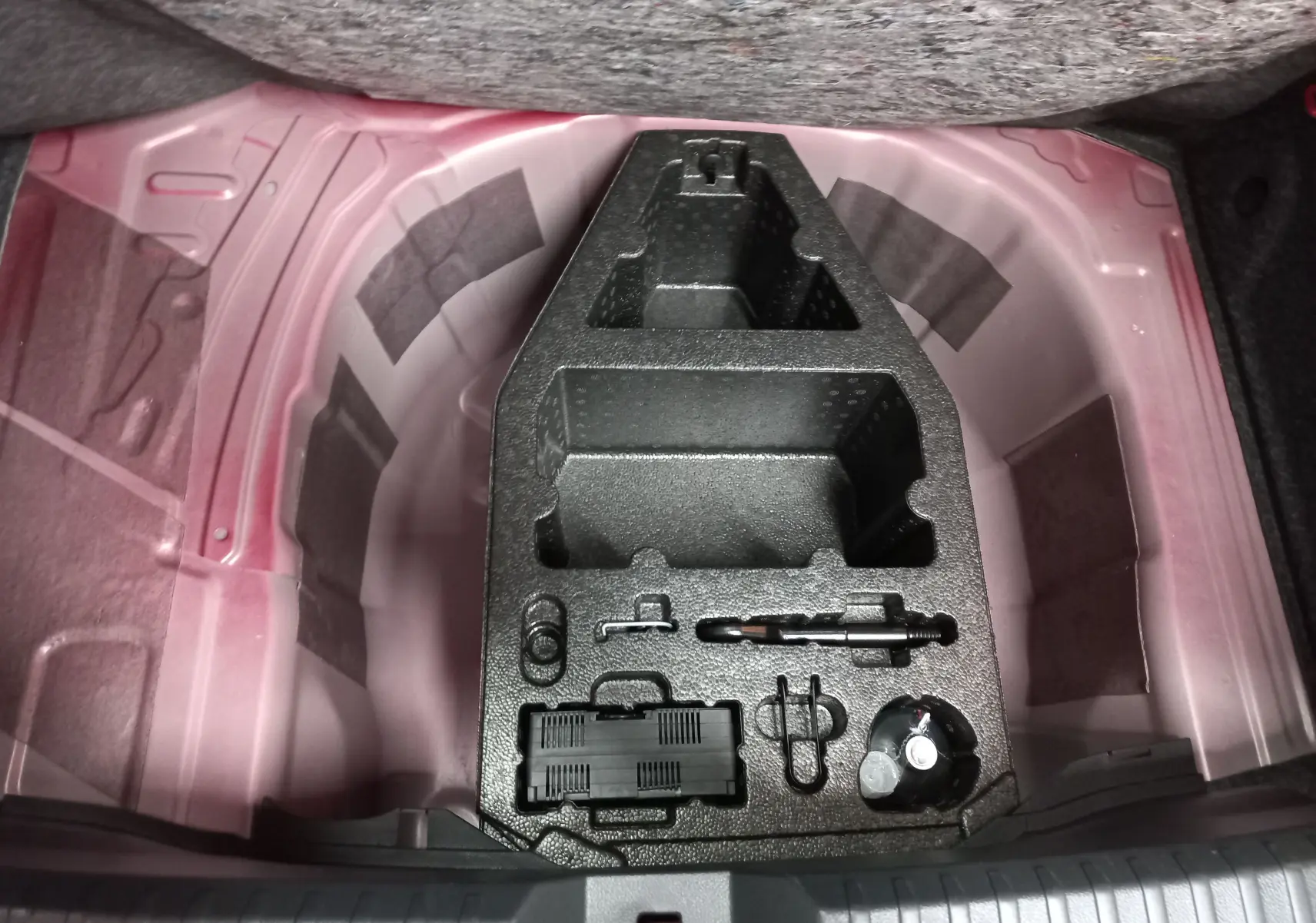 Coffre ouvert d’une SEAT Ibiza 2025 Rouge Désir, vue plongeante sur le rangement sous plancher avec outils intégrés.