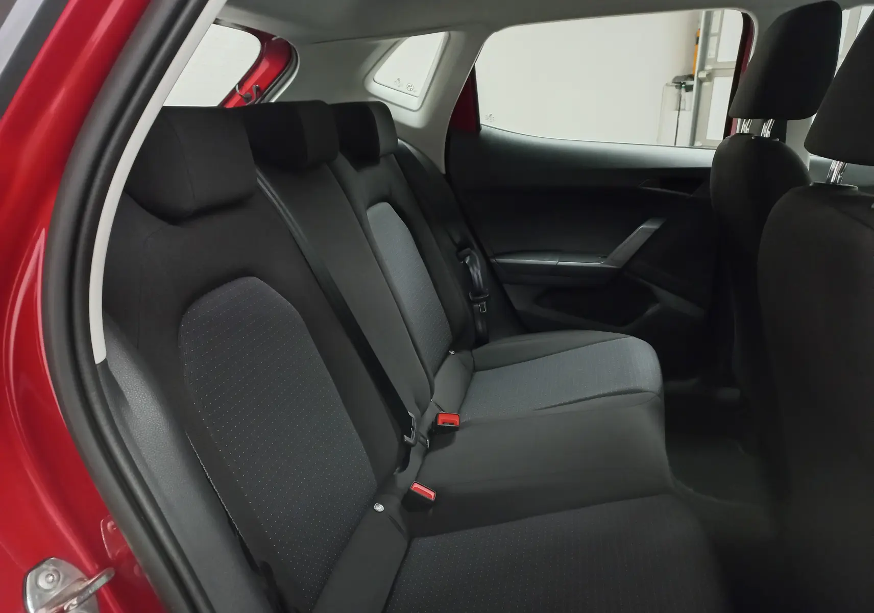 Vue intérieure côté arrière droit de la SEAT IBIZA 2025 rouge désir, montrant les sièges arrière en tissu noir et gris.
