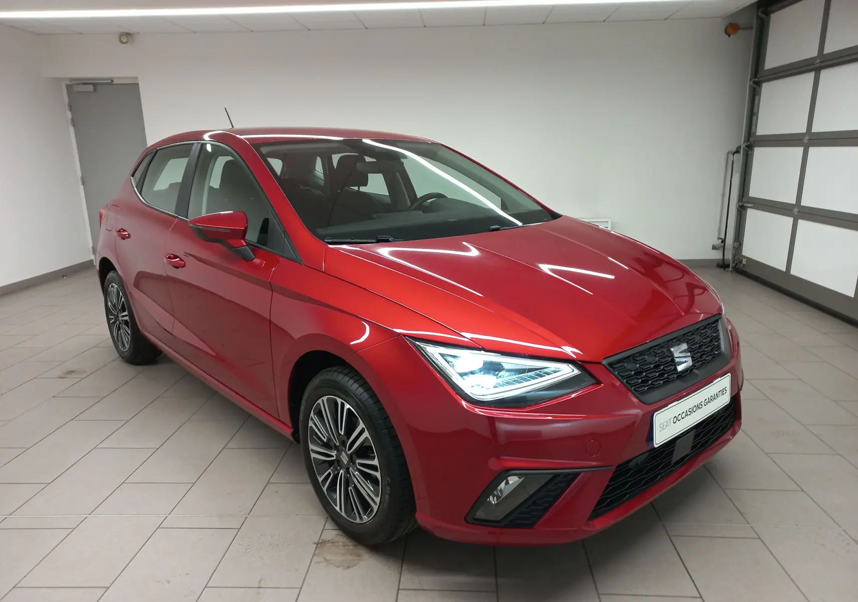 SEAT Ibiza 1.0 TSI 95 Copa rouge désir vue 3/4 avant droit avec phares allumés en intérieur showroom.