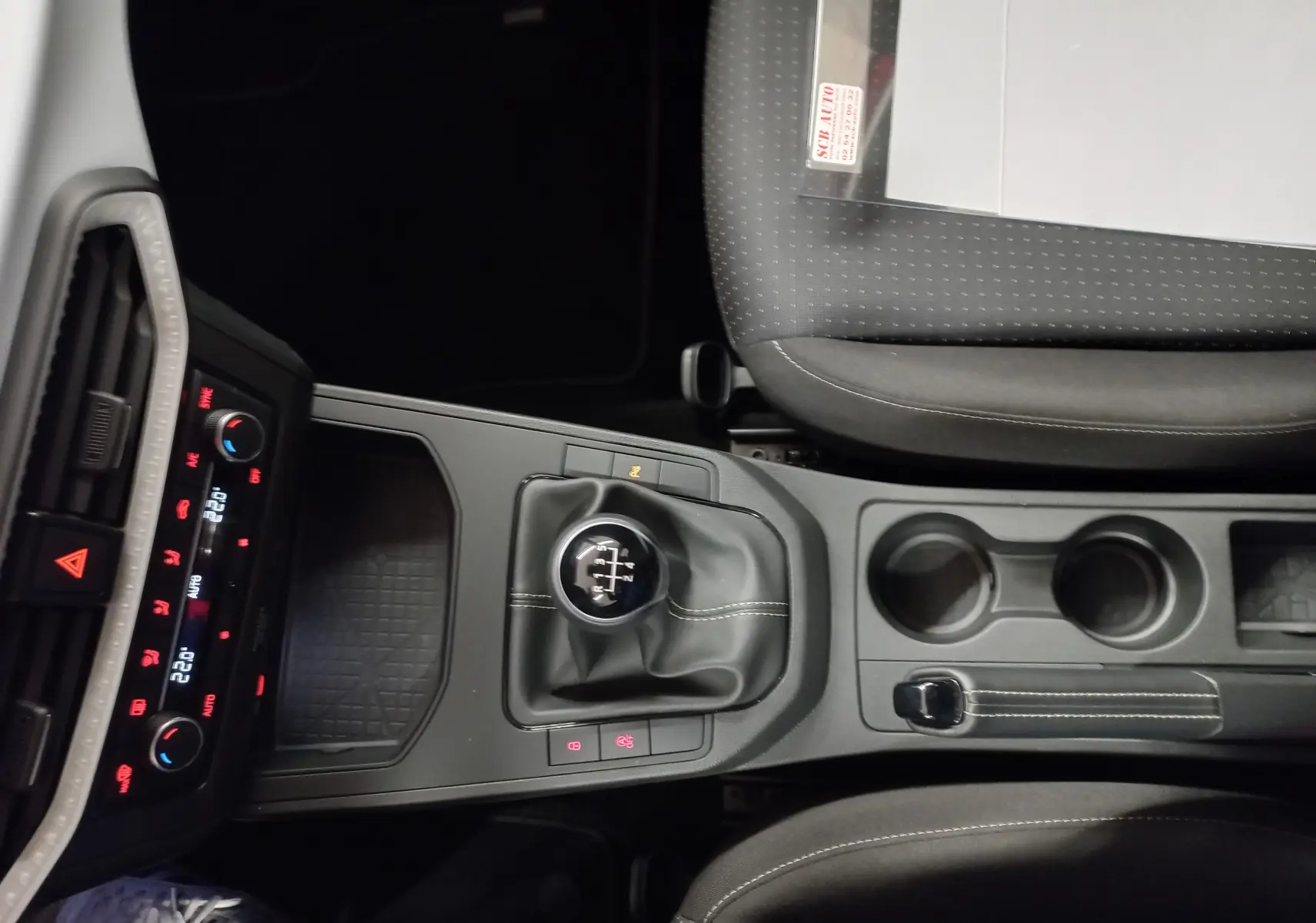 Vue plongeante sur la console centrale de la SEAT IBIZA 2025 rouge désir, avec levier de vitesse manuel et commandes climatisation.