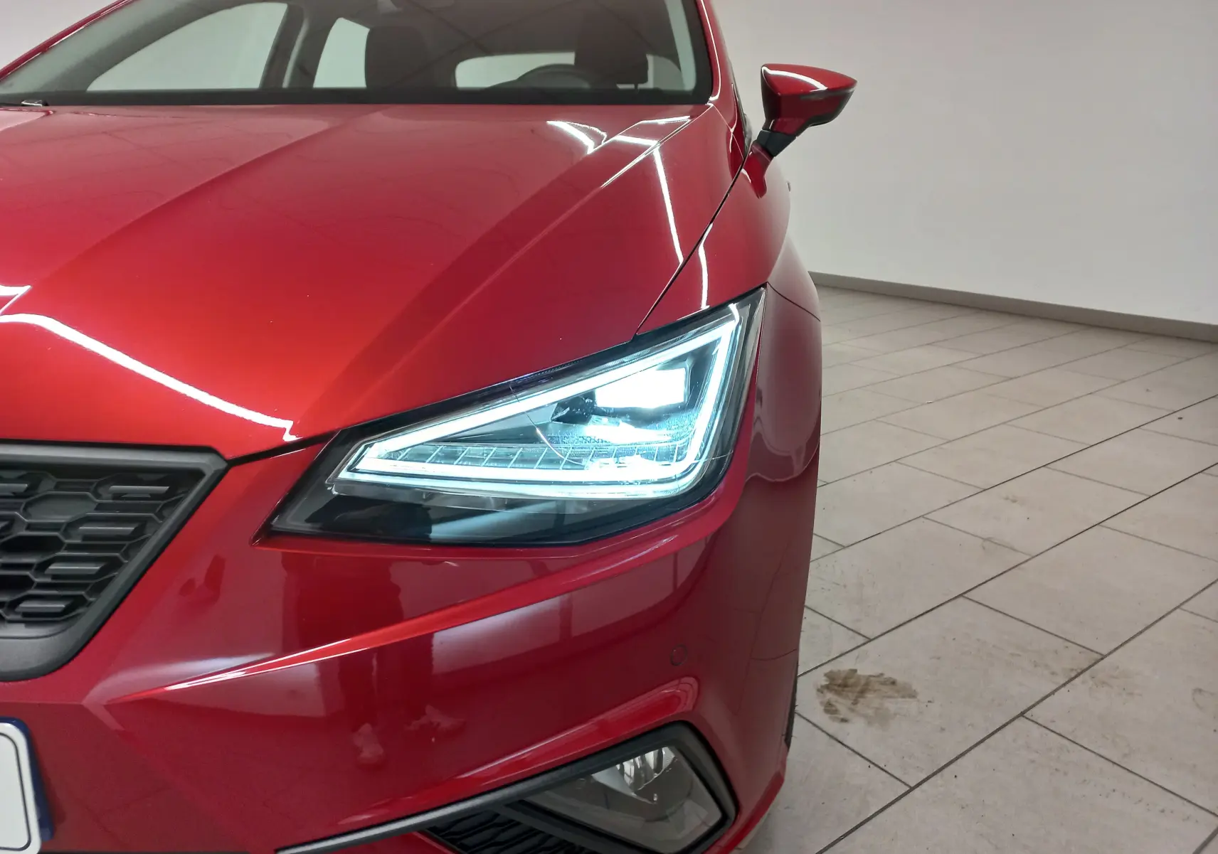 Gros plan sur l'avant droit de la SEAT Ibiza 2025 rouge désir, mettant en valeur son phare LED allumé et la calandre noire.