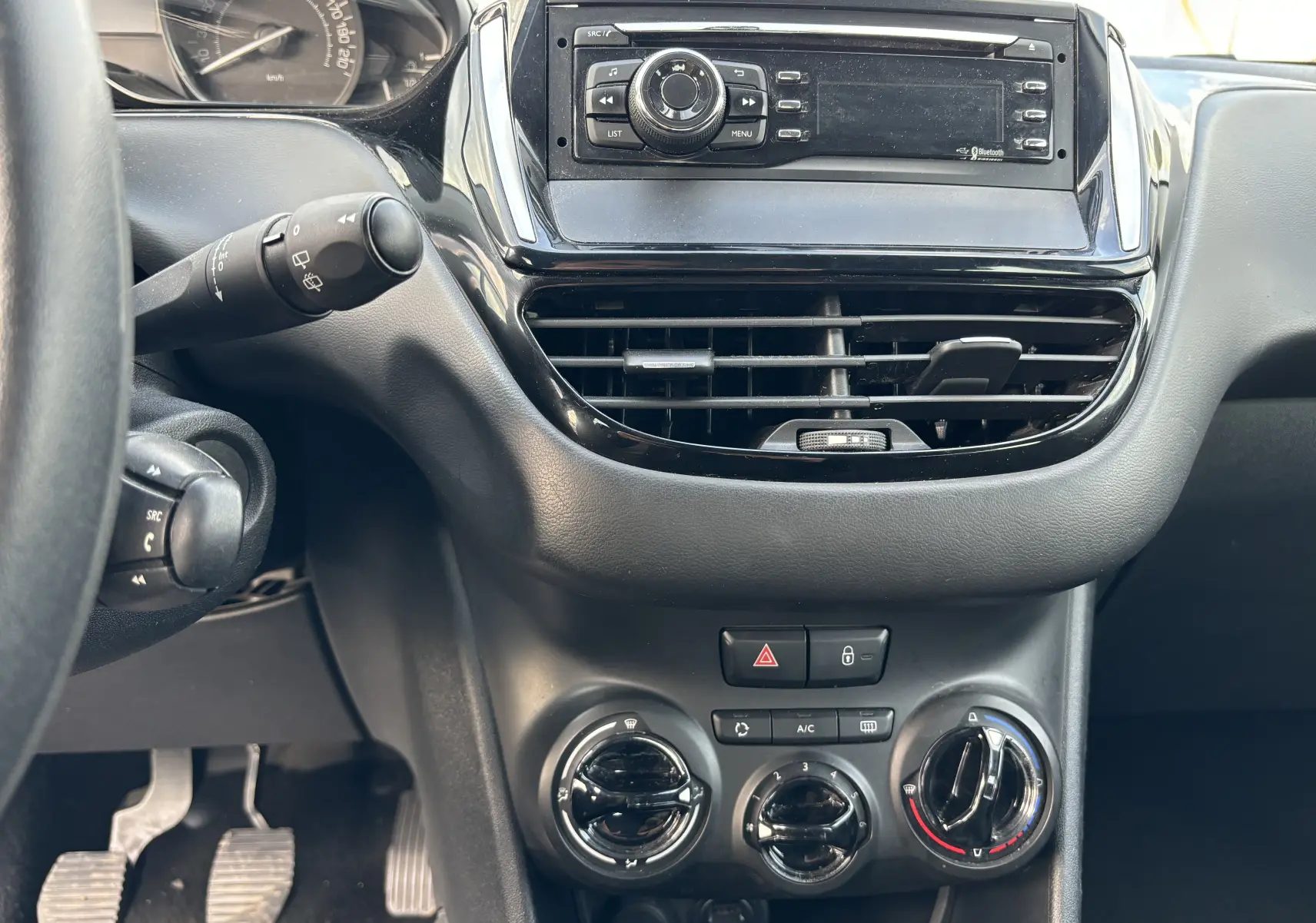 Vue rapprochée du tableau de bord noir et console centrale de la Peugeot 208 gris argent, avec commandes climatisation et radio.