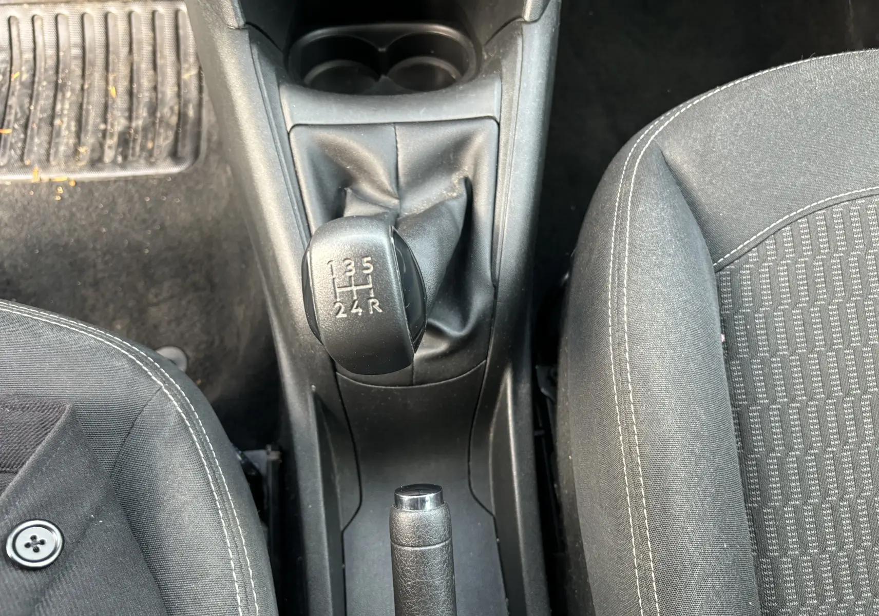 Vue plongeante sur la boîte manuelle et le frein à main entre les sièges en tissu noir d'une Peugeot 208 gris argent.