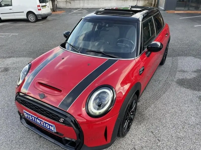 Vue 3/4 avant d'une MINI 5 portes rouge avec toit noir ouvrant et bandes noires sur le capot, roues noires.