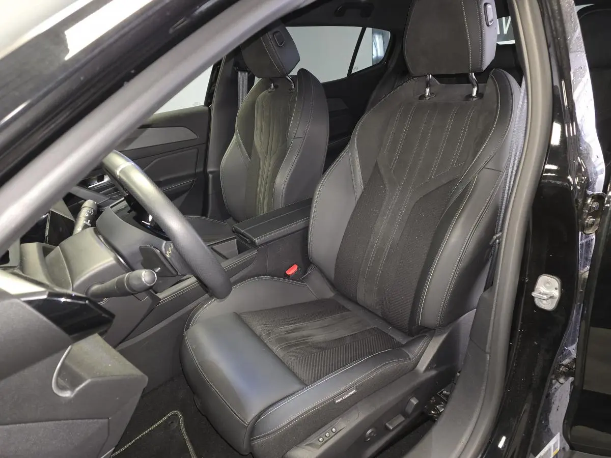 Vue intérieure côté conducteur de la Peugeot 408 GT 1.2i Hybrid 2024, sièges noirs en cuir et tissu avec surpiqûres grises.