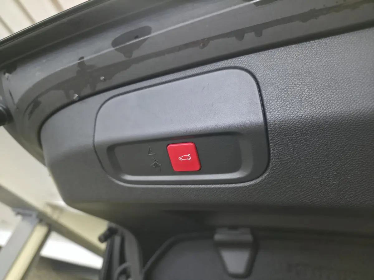 Gros plan sur le bouton rouge d'ouverture électrique du hayon du coffre d'une Peugeot 408 noire.