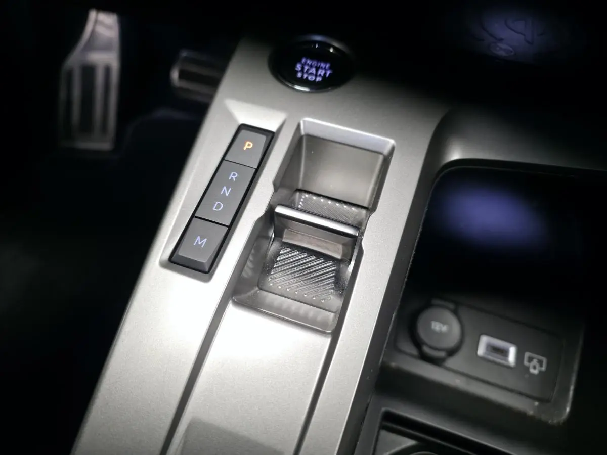 Gros plan sur la console centrale argentée de la Peugeot 408 Hybrid 2024 avec sélecteur de boîte auto et bouton start/stop.