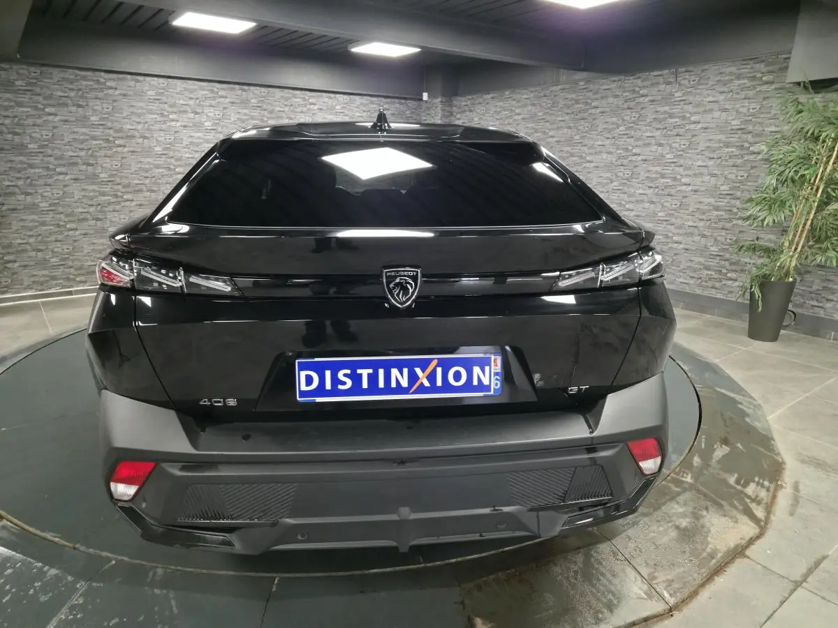 Vue arrière d'une Peugeot 408 noire avec feux arrière fins et logo lion central sur fond noir brillant.