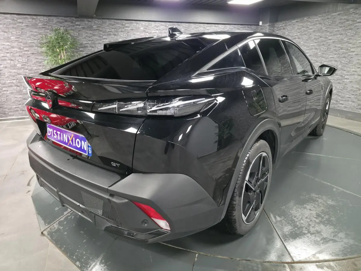 Vue 3/4 arrière droite d'une Peugeot 408 GT noire avec jantes alliage 19 pouces et feux arrière LED griffés.