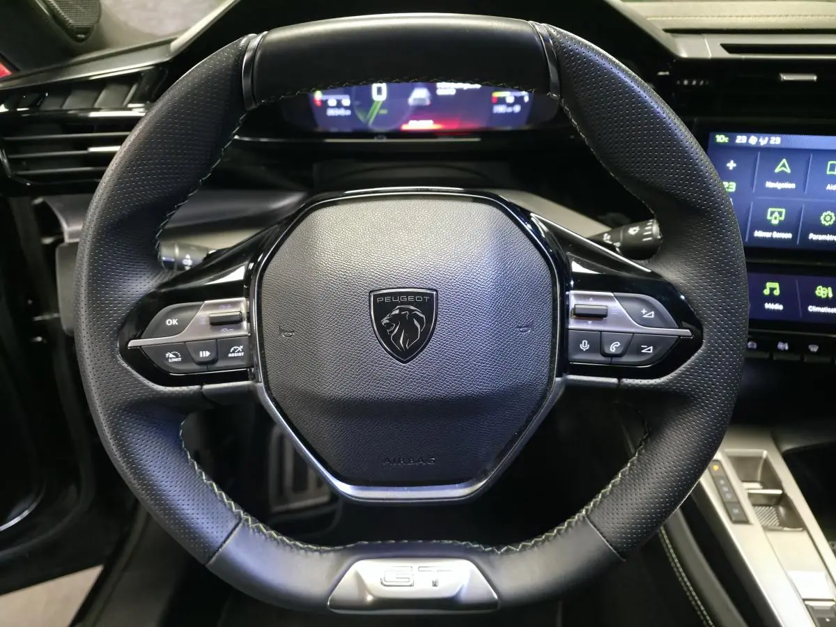 Volant cuir perforé noir de la Peugeot 408 GT 2024 avec commandes intégrées et instrumentation numérique en arrière-plan.