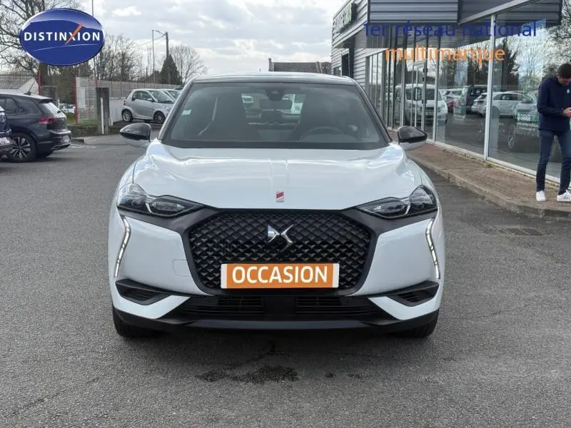 Vue frontale d'une DS3 Crossback blanc perle nacré avec toit noir, calandre noire et feux LED verticaux allumés.