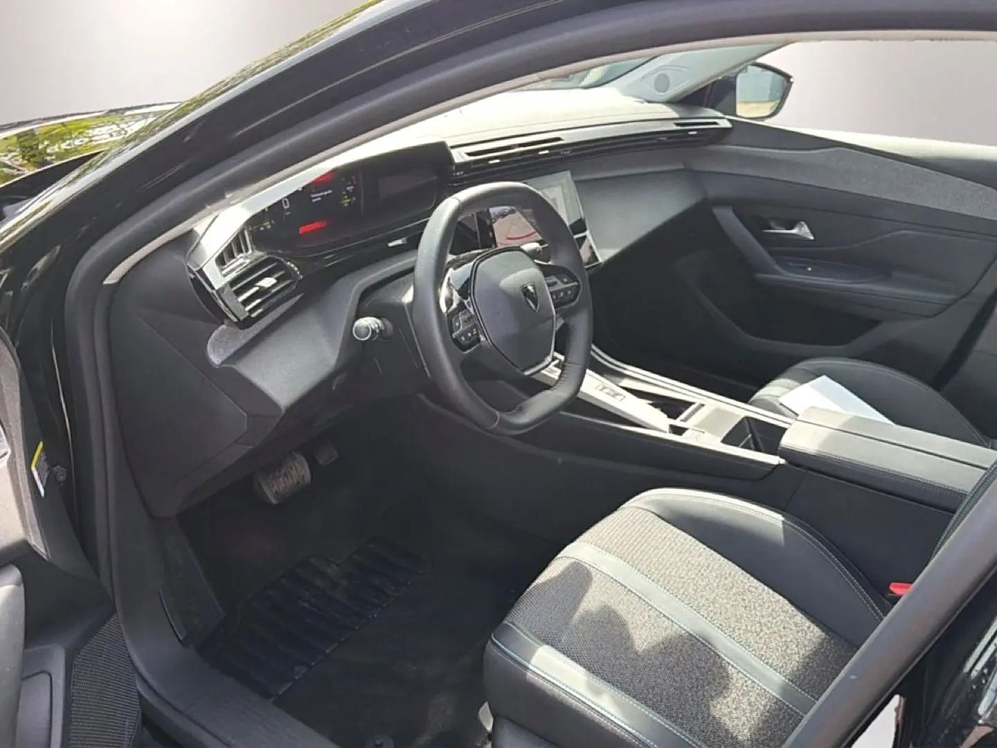 Vue intérieure côté conducteur de la Peugeot 408 Hybrid noire 2024, avec volant cuir et console centrale moderne.