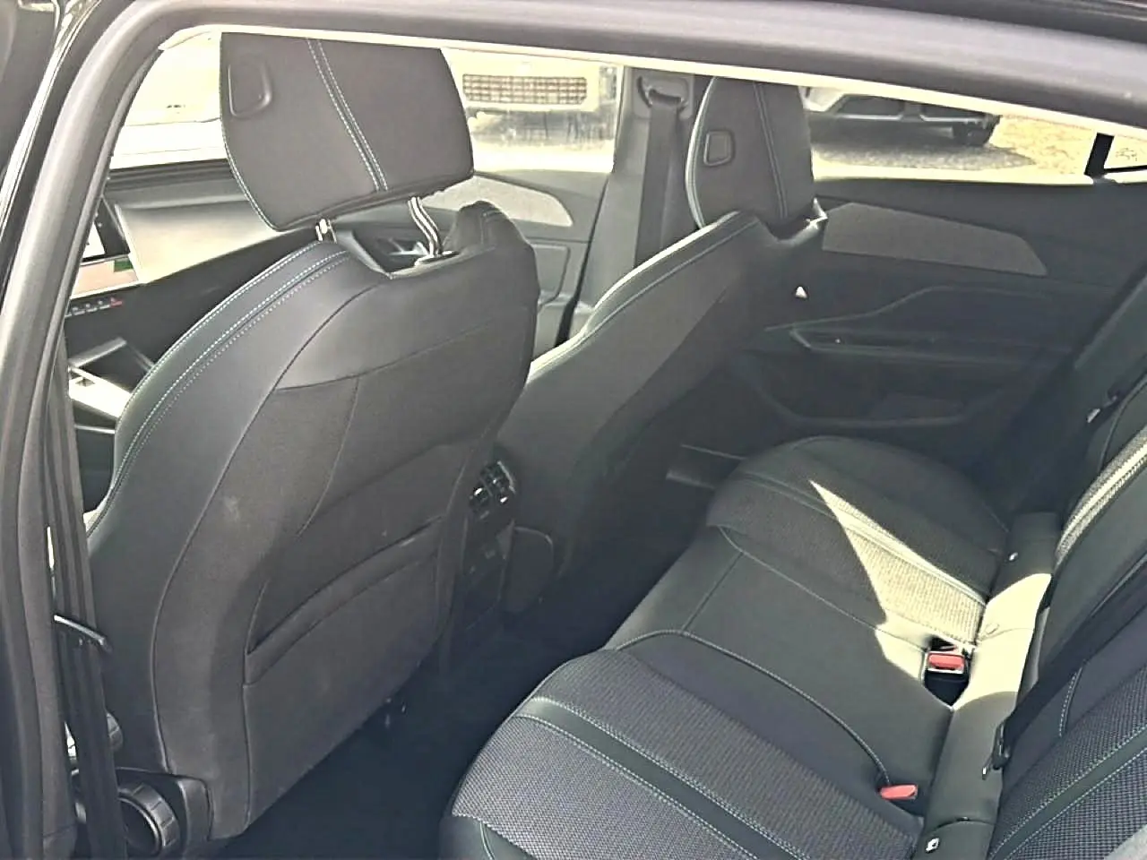 Vue intérieure arrière droite de la Peugeot 408 Hybrid 136 allure e-dcs6 noire, montrant les sièges et les finitions tissu et cuir.