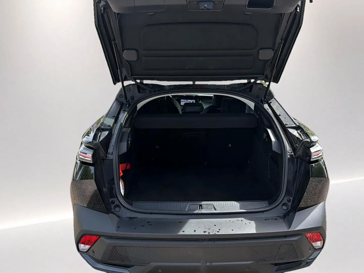 Vue arrière de la Peugeot 408 Hybrid 136 allure e-dcs6 noire avec coffre ouvert montrant l’espace de chargement vide.