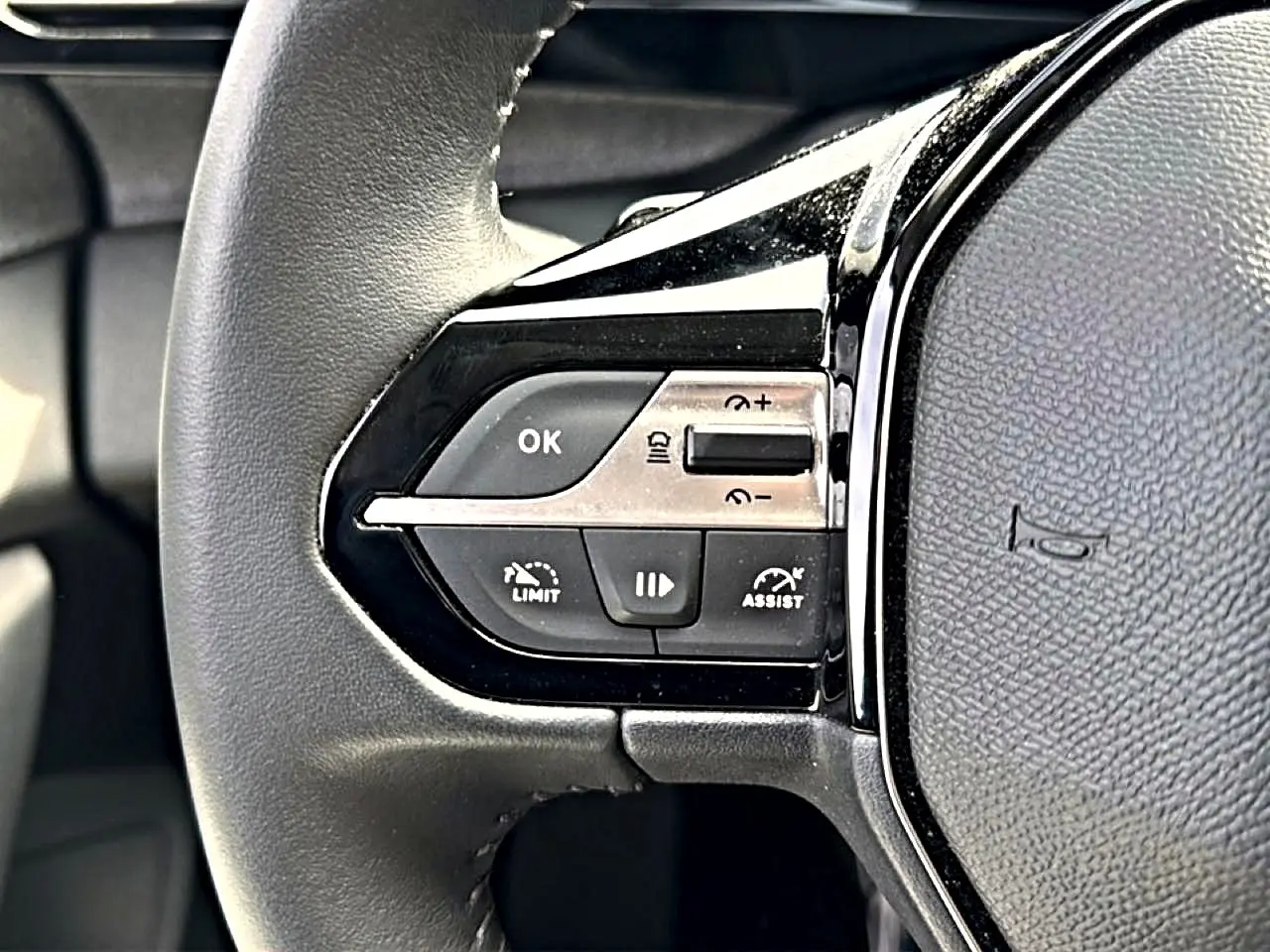 Gros plan sur le côté gauche du volant cuir noir du Peugeot 408 Hybrid 136 allure avec commandes de régulateur et assistant.