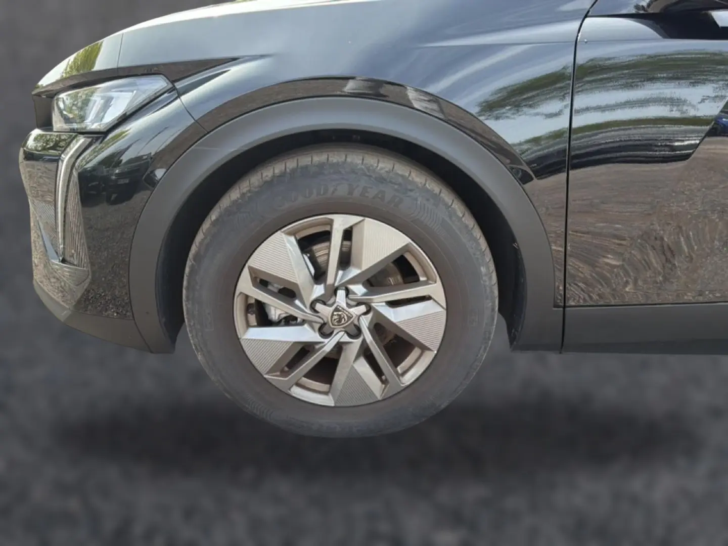Gros plan sur la roue avant gauche noire d’une Peugeot 408 Hybrid 136 allure 2024 avec jante alu et phare LED partiel.