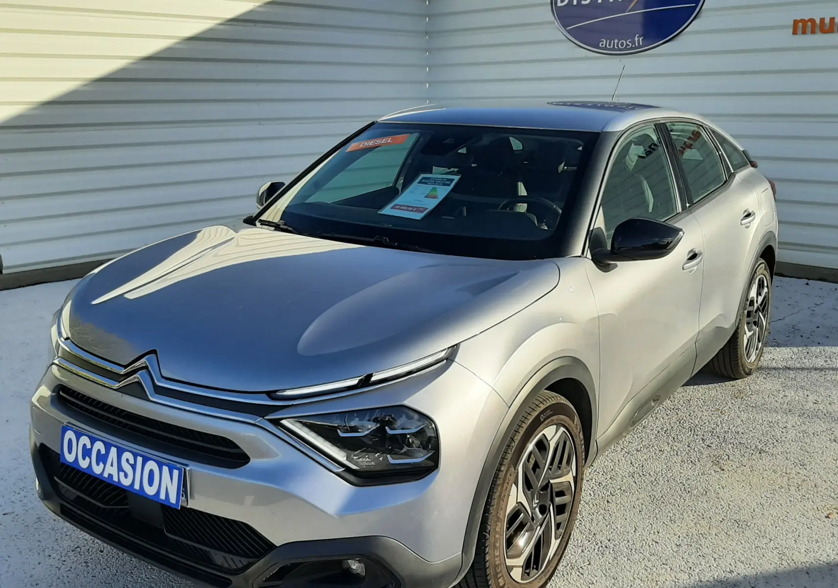 Citroën C4 gris vue 3/4 avant droit, avec calandre distinctive et jantes bi-ton, stationnée devant un mur blanc.