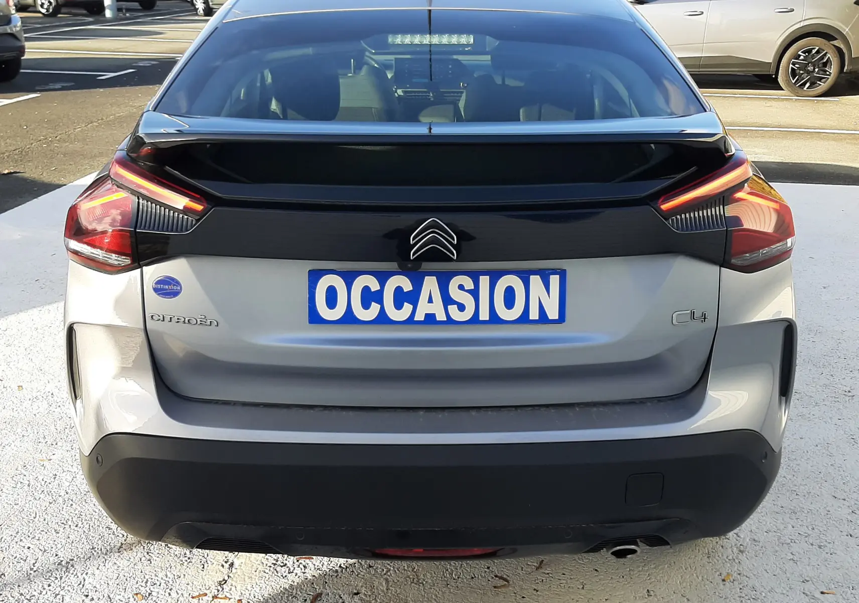 Vue arrière d'une Citroën C4 gris clair 2023 avec feux LED et logo distinctif sur un parking.