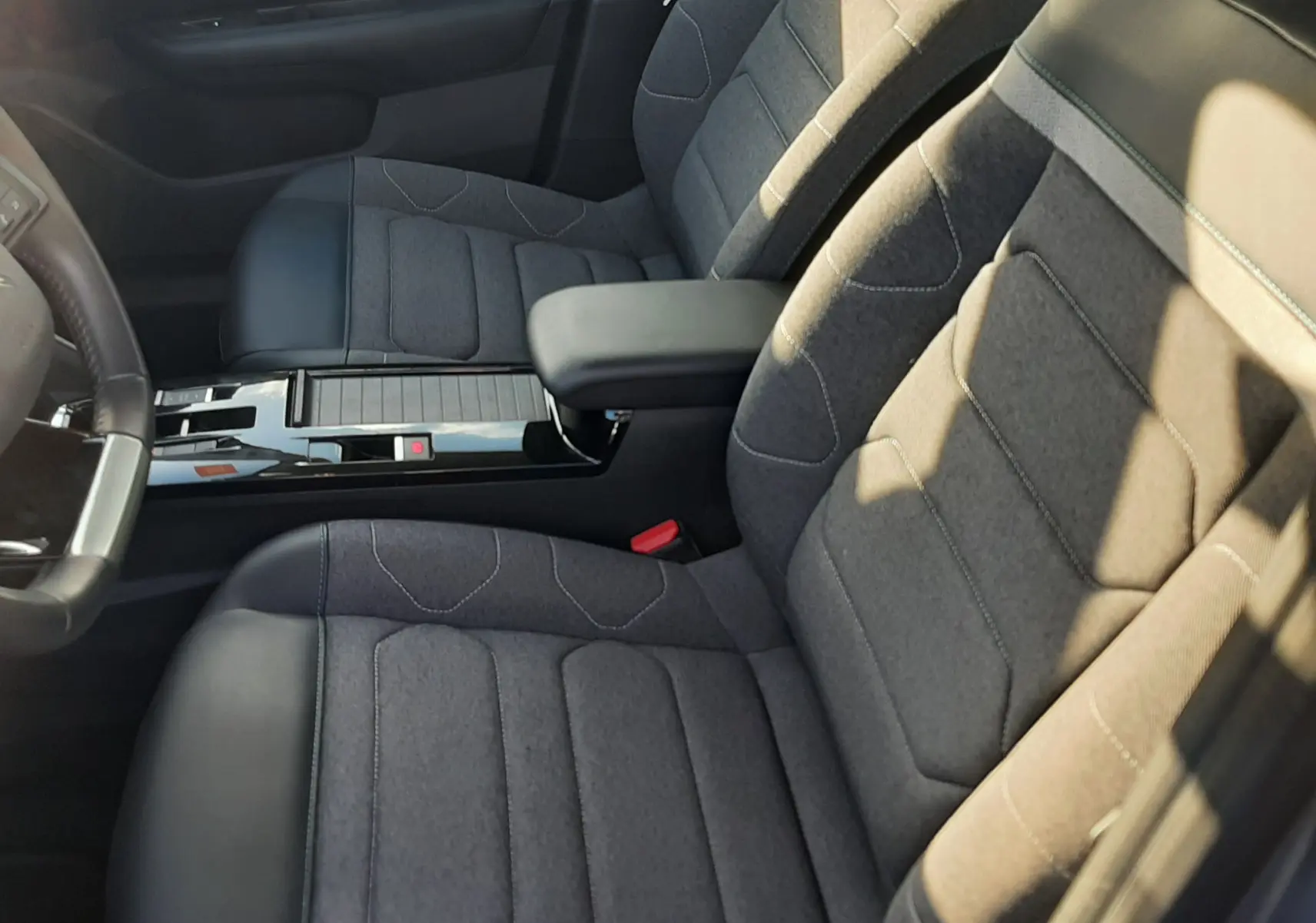 Vue intérieure côté avant droit de la Citroën C4 gris 2023, sièges tissu gris avec surpiqûres et accoudoir central noir.
