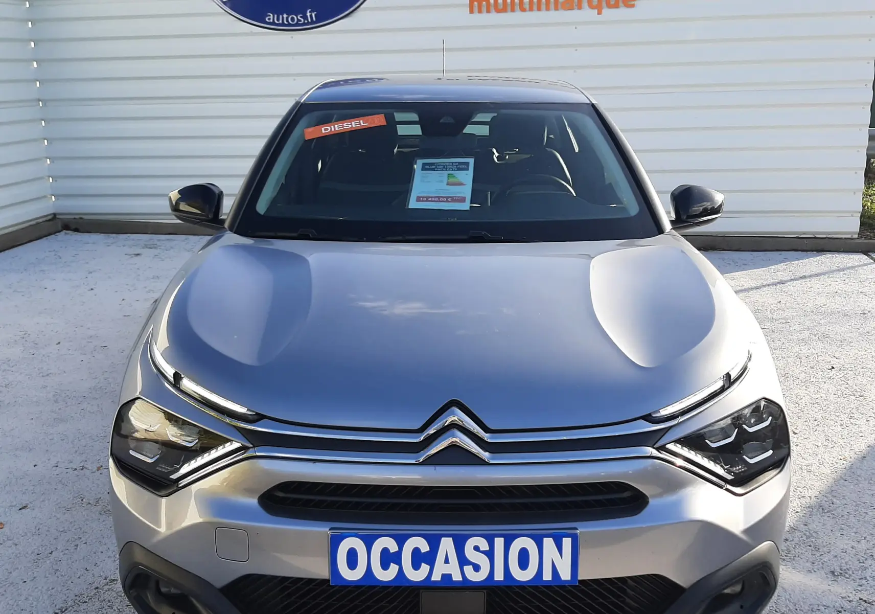 Vue avant d'une Citroën C4 gris métallisé 2023 avec plaque "OCCASION" et autocollant "DIESEL" sur le pare-brise.