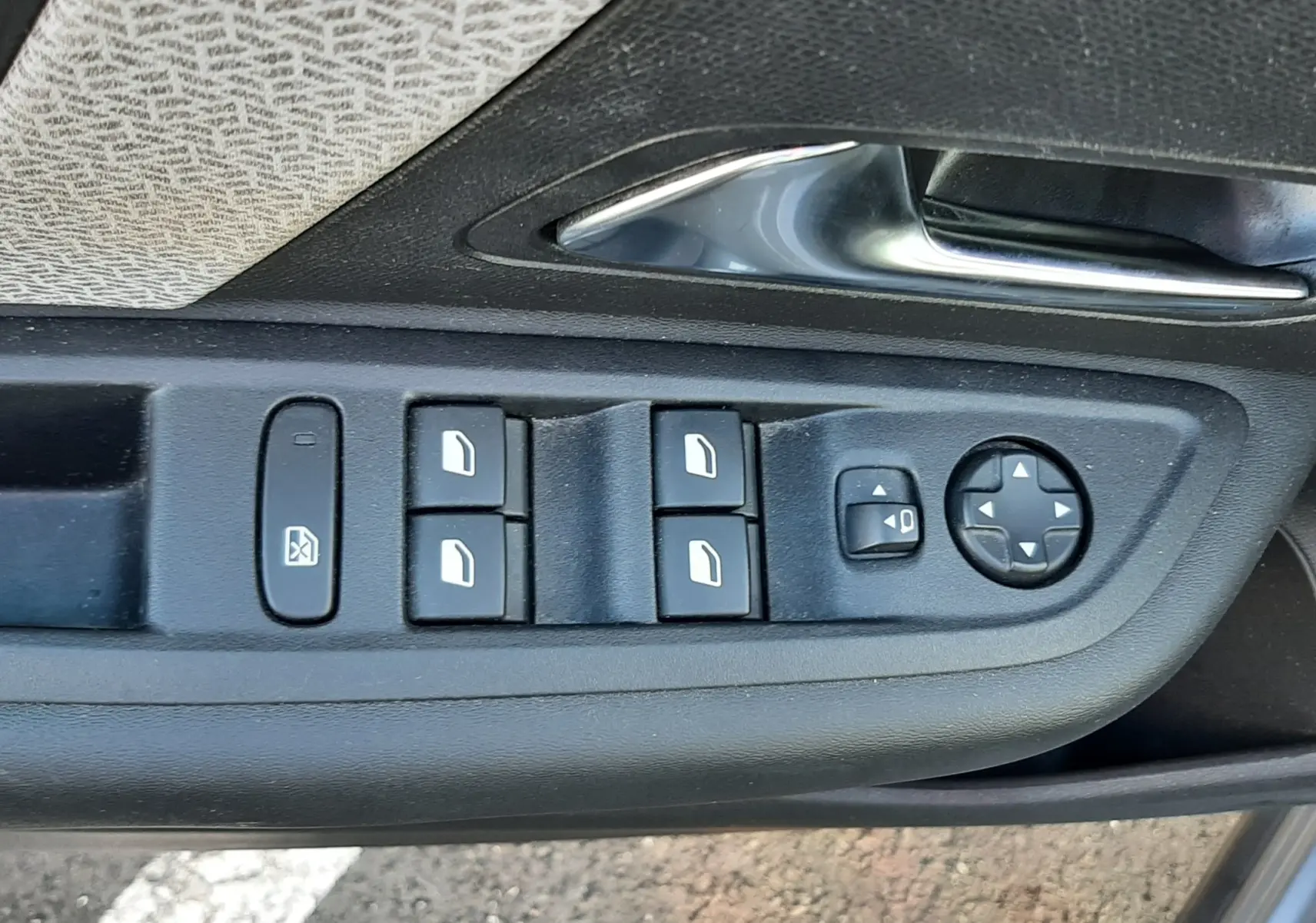 Gros plan sur la commande des vitres et rétroviseurs côté conducteur d'une Citroën C4 gris 2023, avec poignée chromée.
