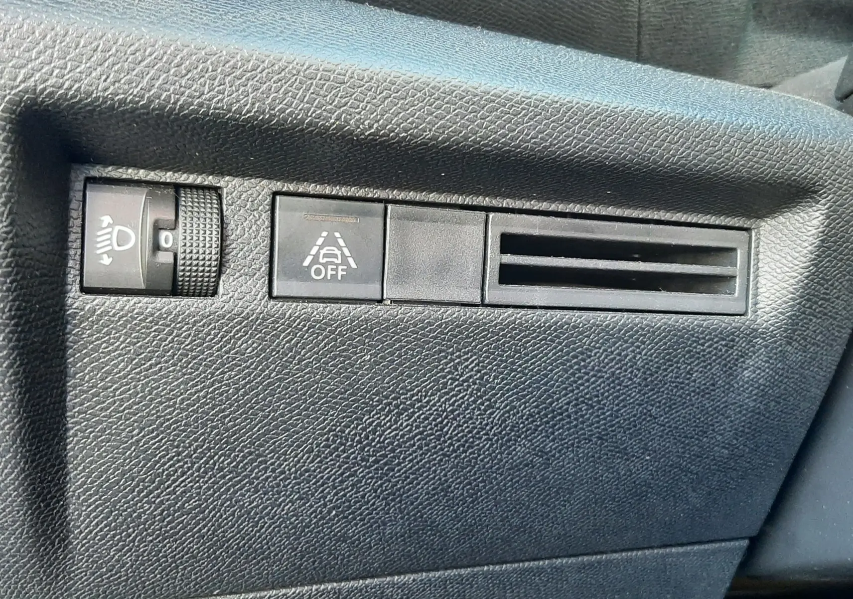 Détail intérieur côté gauche du tableau de bord gris d'une Citroën C4 2023 avec commandes de réglage des phares et d'alerte de franchissement de ligne.