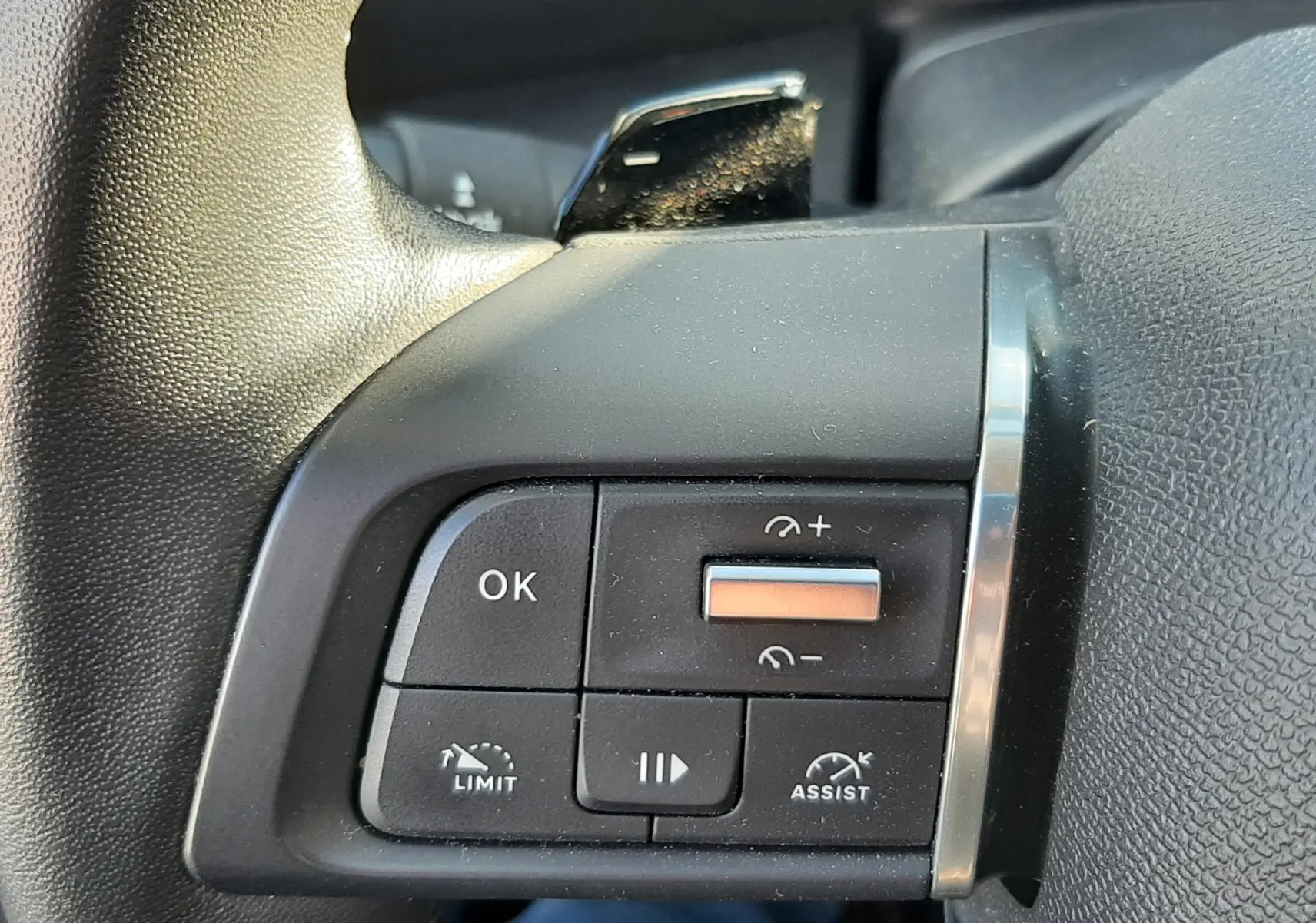 Gros plan sur les commandes gauche du volant noir de la Citroën C4 gris 2023, avec boutons de régulateur et limitation de vitesse.