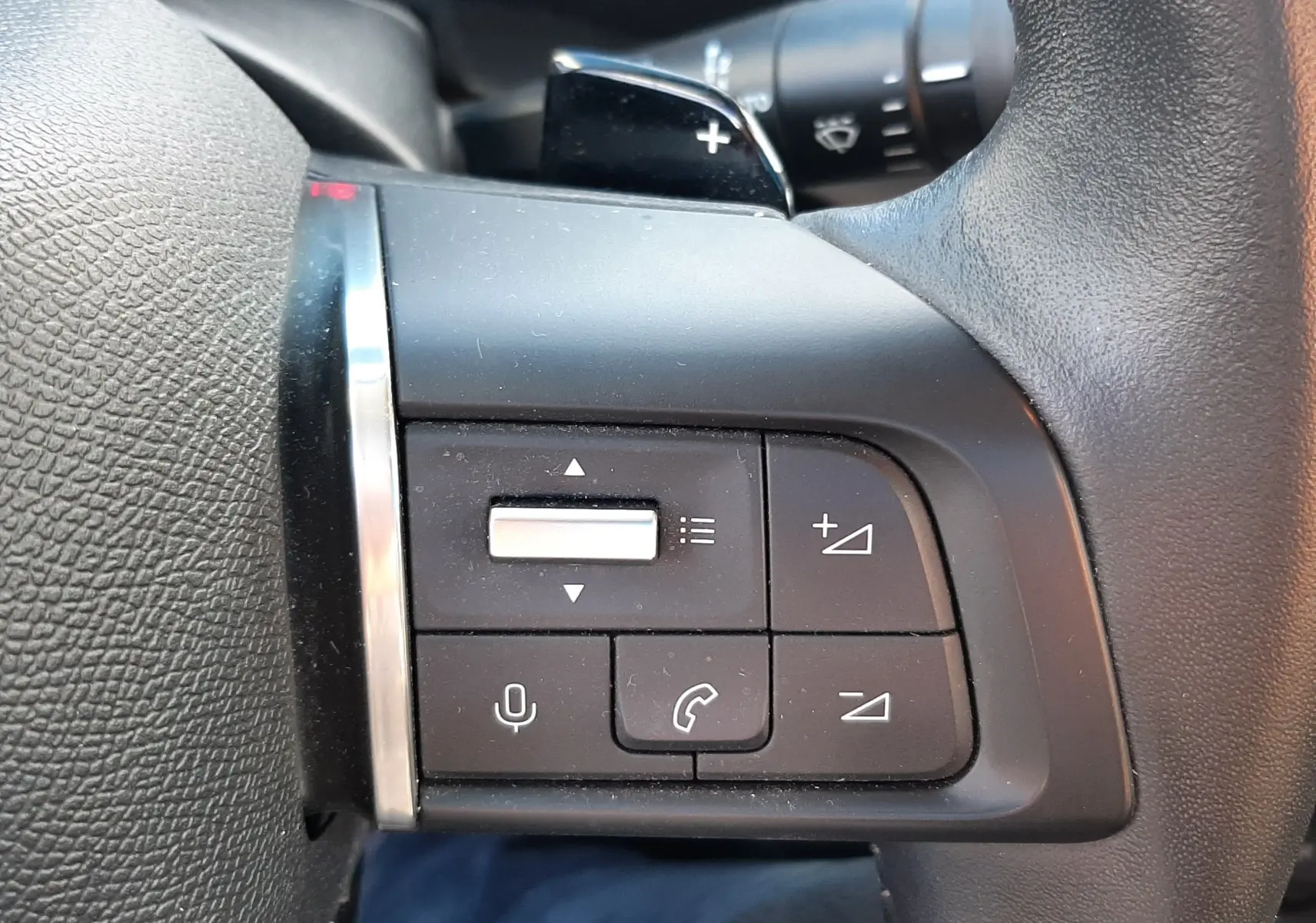 Gros plan sur les commandes de volume et téléphone au volant noir du Citroën C4 gris 2023, version BlueHDi 130ch Feel Pack.