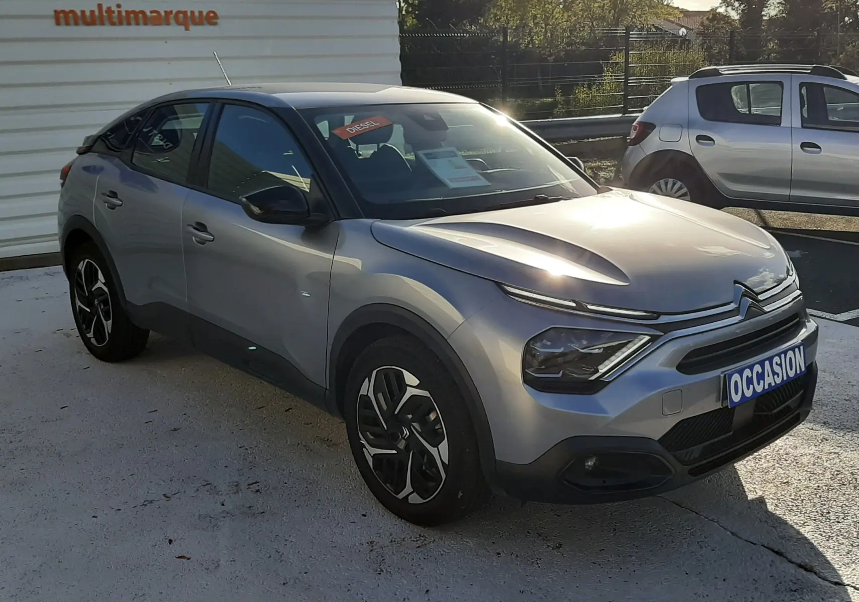 Vue 3/4 avant d'une Citroën C4 gris métallisé 2023 avec jantes bicolores et plaque "OCCASION" visible.