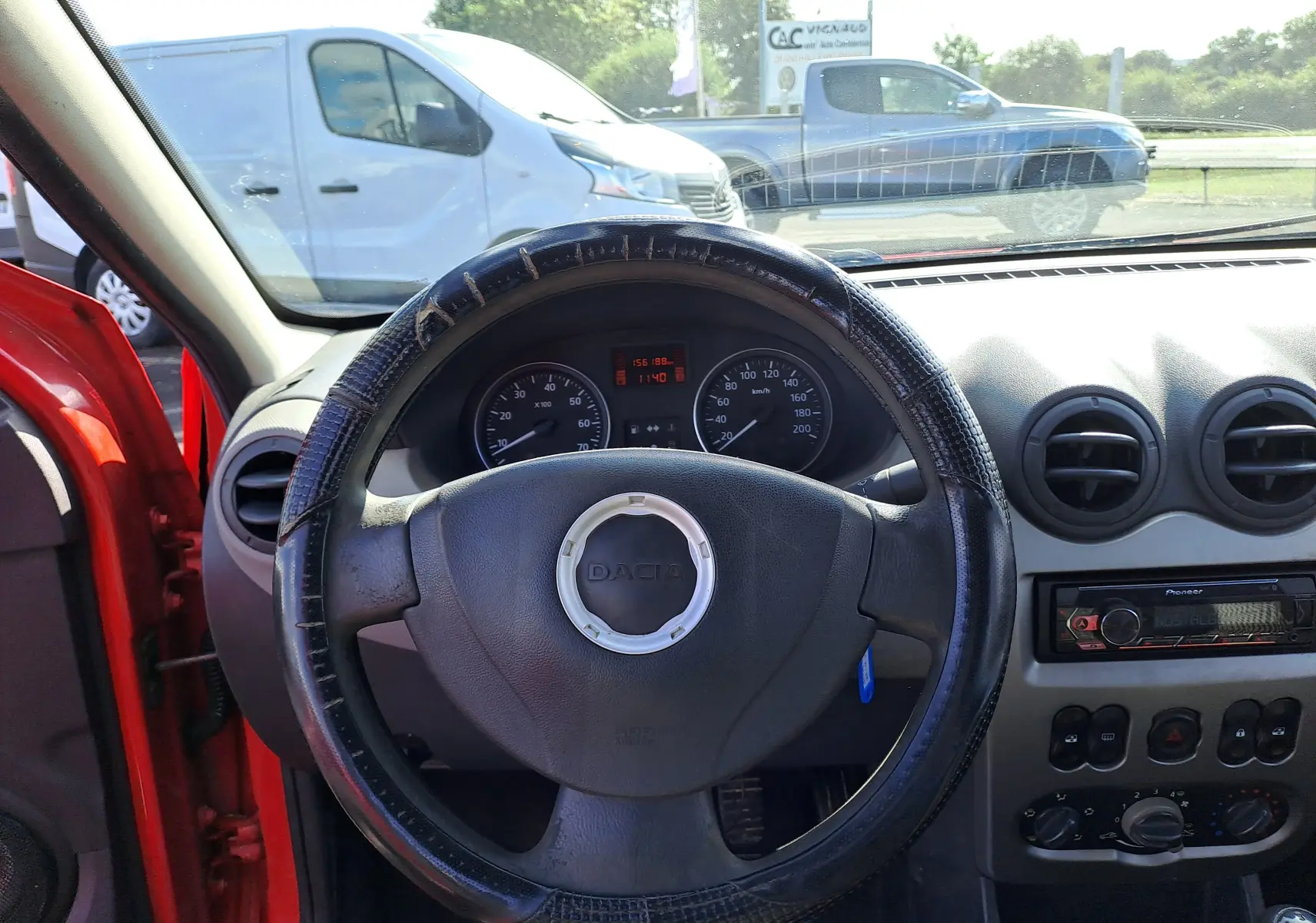 Vue intérieure du volant et tableau de bord d'une Dacia Sandero rouge de 2010 avec commandes et autoradio visibles.