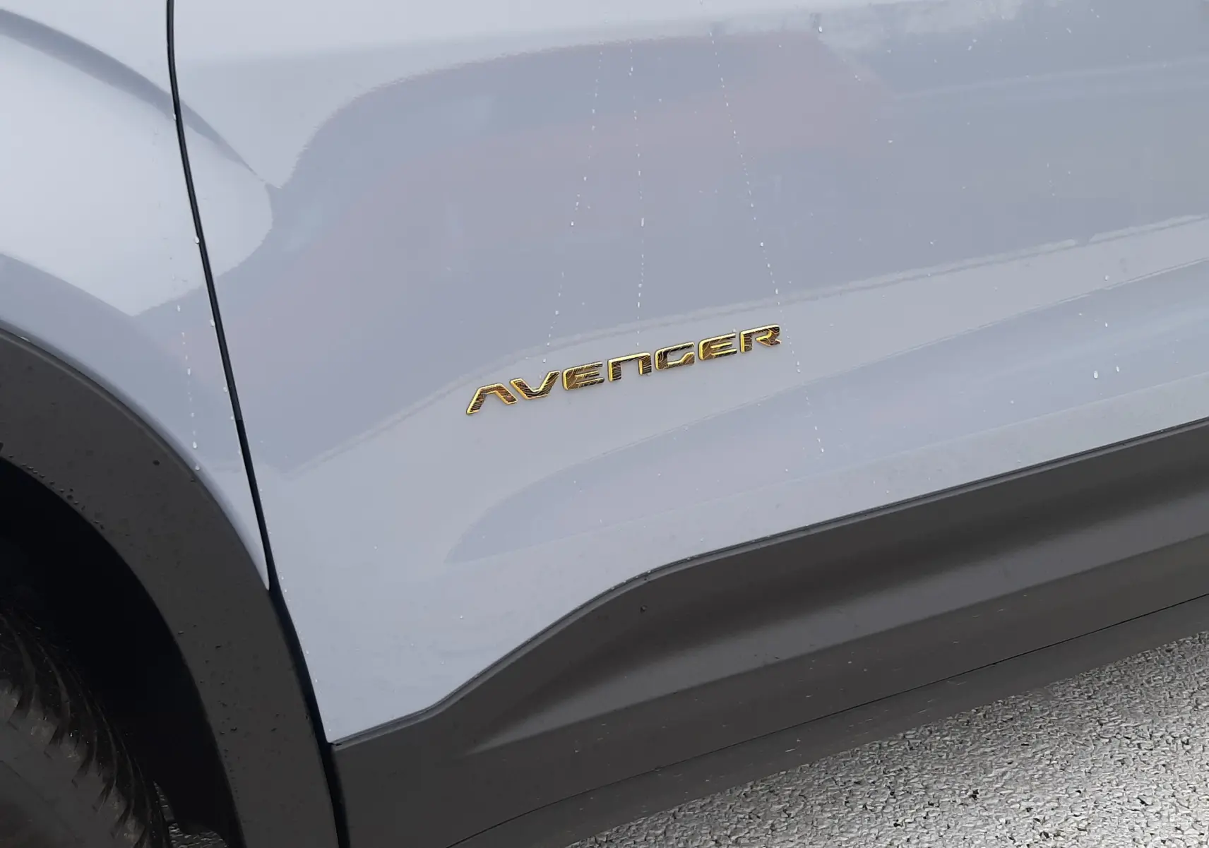 Gros plan sur le côté gauche gris Storm du Jeep Avenger avec le logo doré Avenger visible sur la portière.