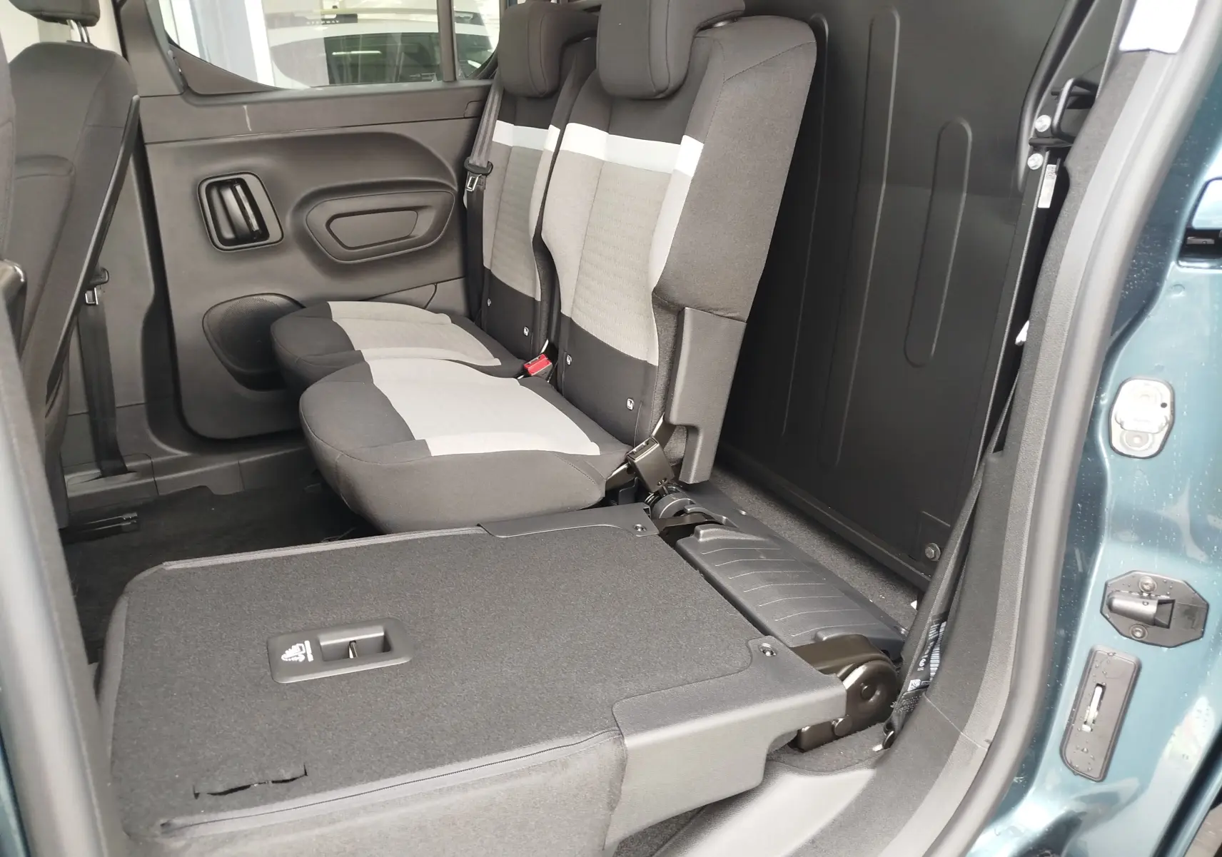 Vue intérieure côté droit du Citroën Berlingo bleu Kiarma 2025, montrant la banquette arrière grise et noire partiellement rabattue.