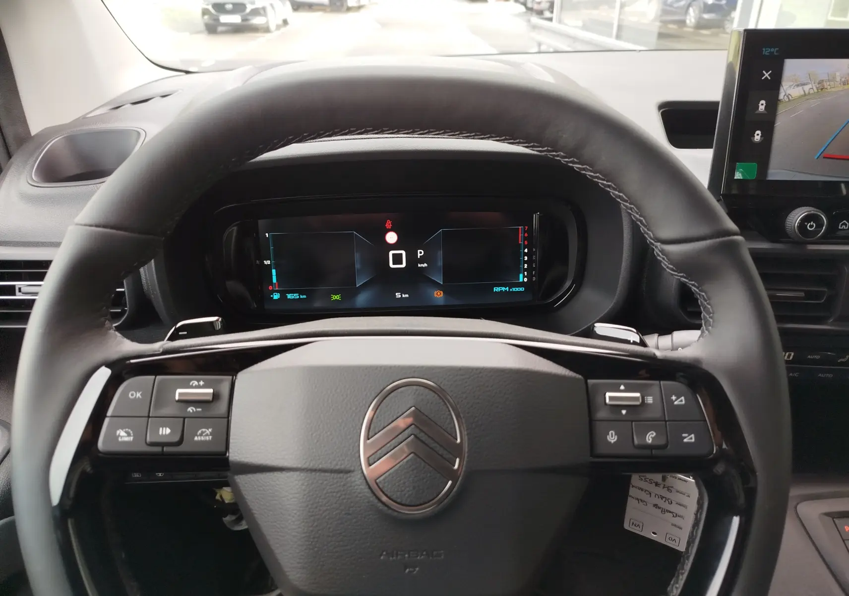 Vue intérieure centrée sur le volant noir du Citroën Berlingo 2025 avec tableau de bord numérique et écran de caméra de recul.