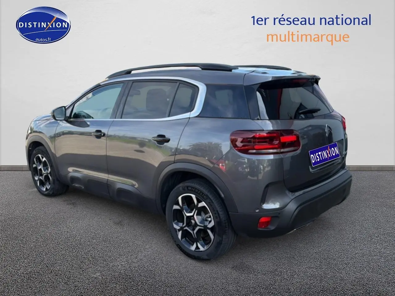 Vue 3/4 arrière droit d'un Citroën C5 Aircross gris platinium avec barres de toit et jantes alu noires.