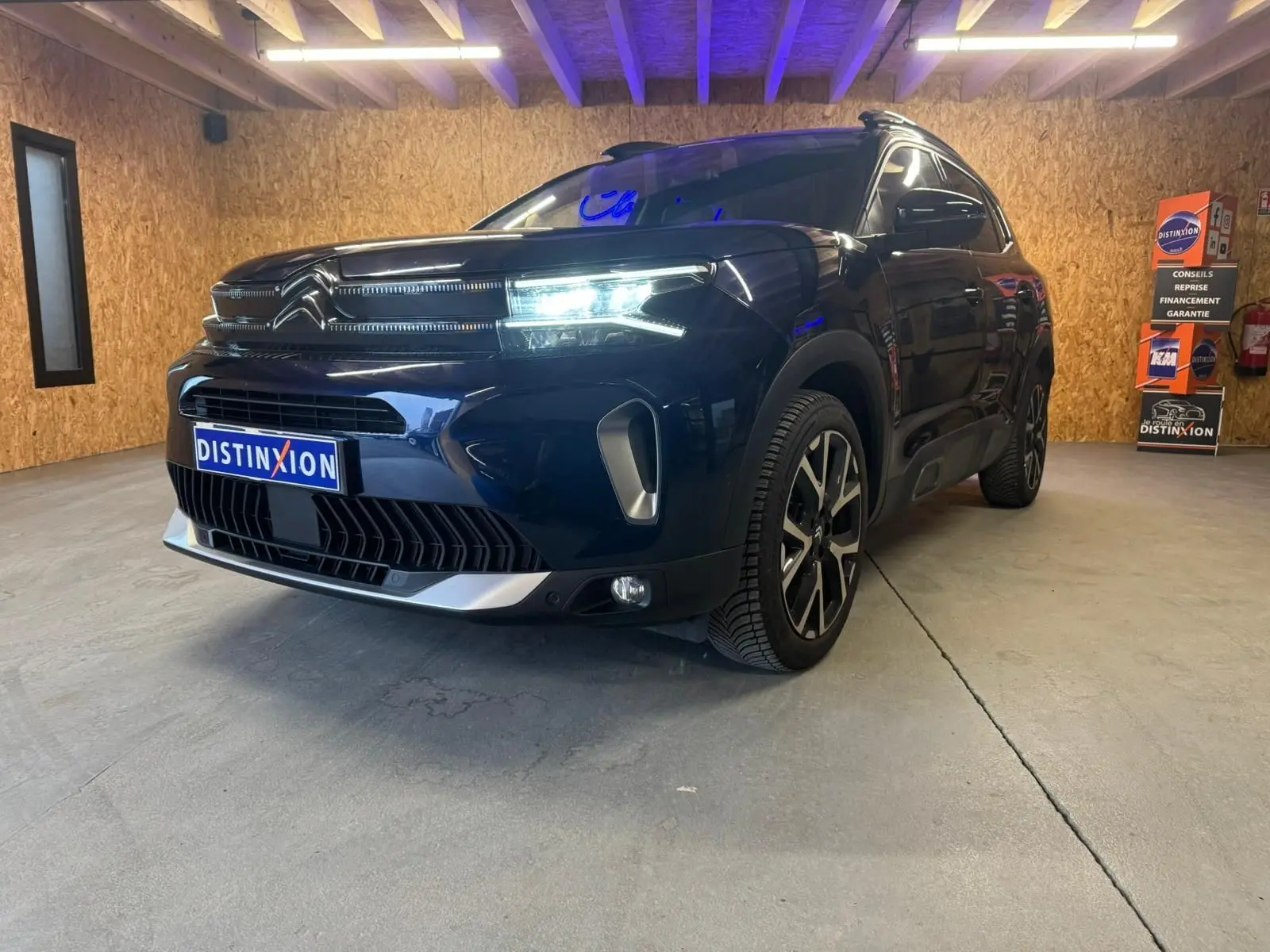 Vue 3/4 avant droite du Citroën C5 Aircross bleu avec barres de toit et jantes alu 18 pouces dans un showroom.