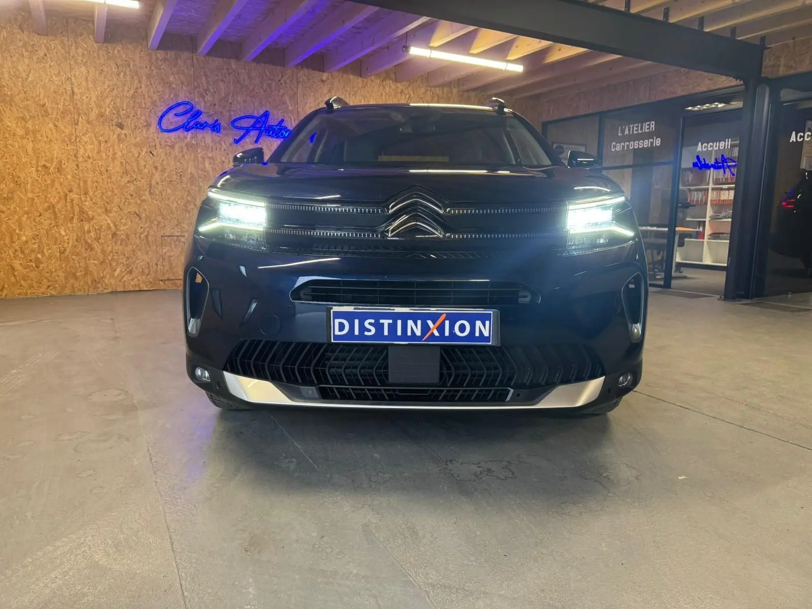 Vue de face du Citroën C5 Aircross bleu avec phares LED allumés et barres de toit visibles en intérieur showroom.