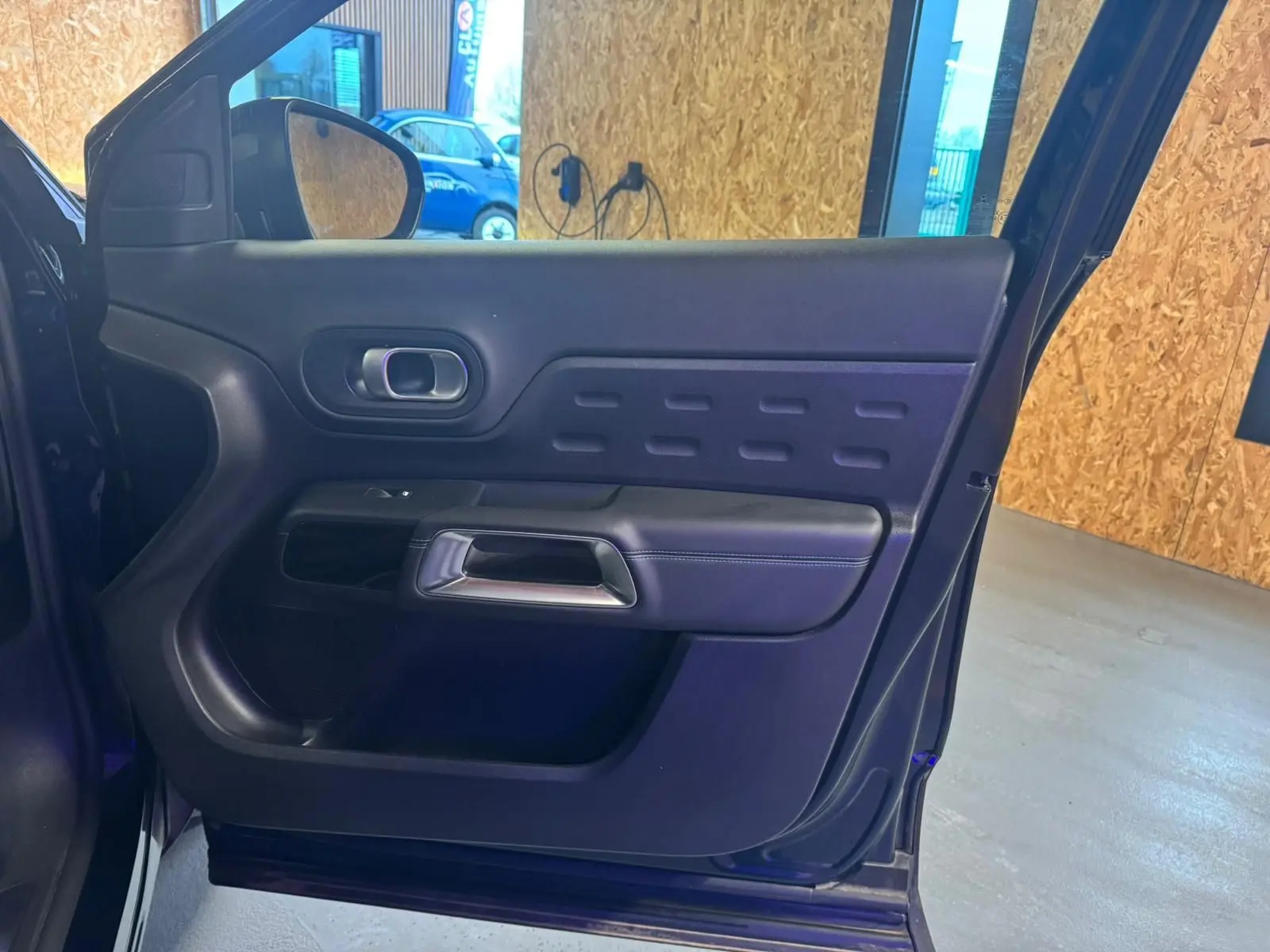 Vue intérieure côté gauche de la porte avant d’un Citroën C5 Aircross bleu avec poignée argentée et panneau noir texturé.