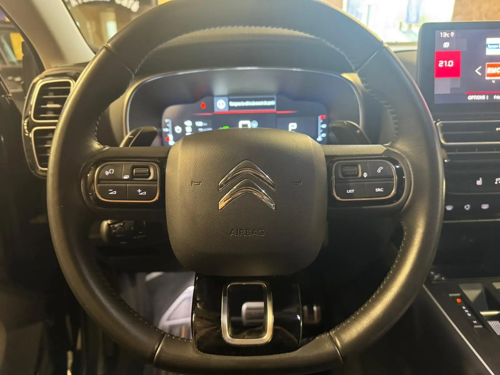 Gros plan sur les commandes noires du volant en cuir du Citroën C5 Aircross, avec écran numérique en arrière-plan.